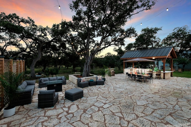 patio terrace at dusk with a gazebo, an outdoor living space, outdoor dining area, and fence