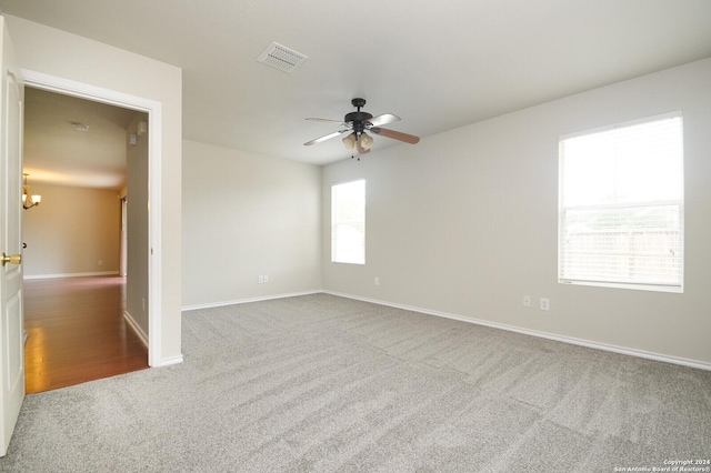 carpeted empty room featuring ceiling fan with notable chandelier, baseboards, and visible vents