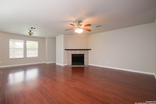 unfurnished living room with a tiled fireplace, dark hardwood / wood-style flooring, and ceiling fan