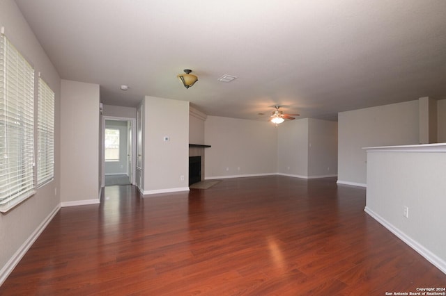 unfurnished living room with dark wood-type flooring, ceiling fan, baseboards, and a fireplace with flush hearth
