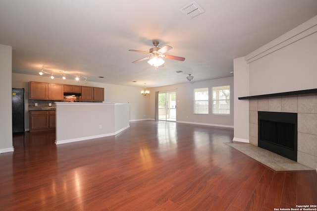 unfurnished living room with a fireplace, baseboards, ceiling fan with notable chandelier, visible vents, and dark wood-type flooring