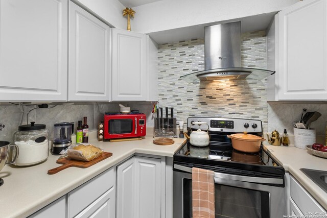 kitchen with wall chimney exhaust hood, white cabinetry, electric range, and decorative backsplash