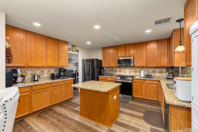 kitchen featuring hardwood / wood-style flooring, decorative light fixtures, a center island, and appliances with stainless steel finishes