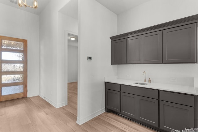 kitchen featuring a sink, light wood finished floors, a notable chandelier, and light countertops