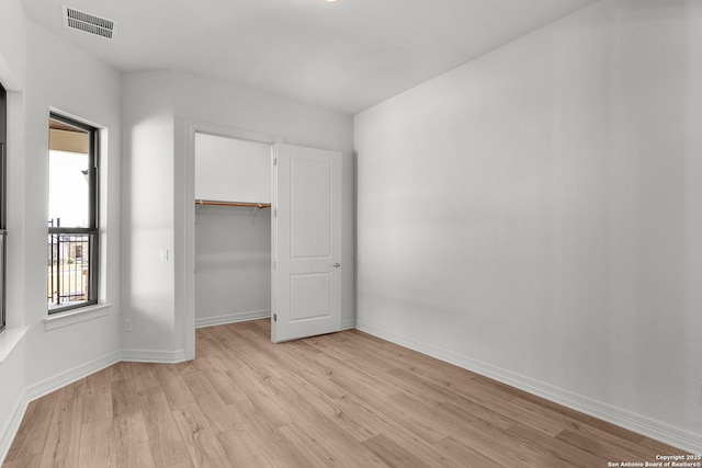 unfurnished bedroom featuring a spacious closet, baseboards, visible vents, and light wood finished floors