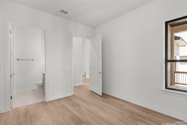 unfurnished bedroom featuring wood finished floors, visible vents, ensuite bathroom, and baseboards