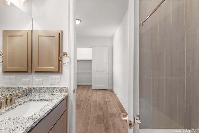 bathroom featuring vanity, wood finished floors, baseboards, and a shower