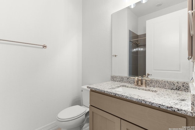 bathroom featuring baseboards, toilet, vanity, and a tile shower