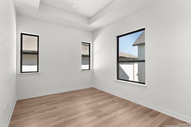 unfurnished room featuring light wood-type flooring, a raised ceiling, and baseboards