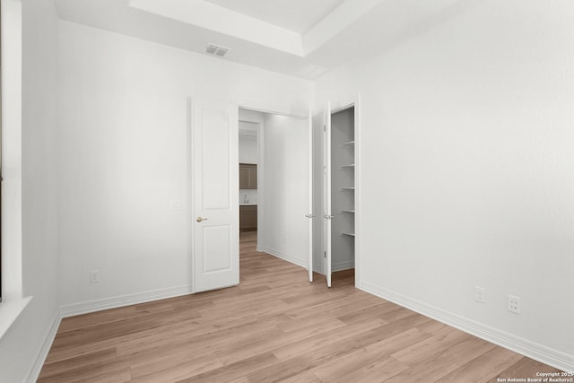 unfurnished bedroom with visible vents, baseboards, light wood finished floors, a tray ceiling, and a closet