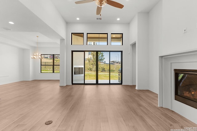 unfurnished living room featuring baseboards, light wood-type flooring, recessed lighting, a high ceiling, and a glass covered fireplace