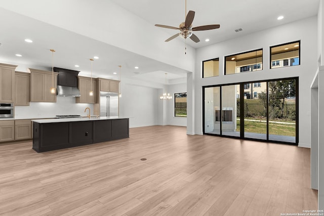 kitchen with light wood finished floors, stainless steel appliances, light countertops, under cabinet range hood, and open floor plan