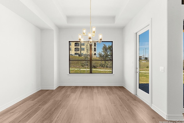 unfurnished dining area featuring a raised ceiling, baseboards, light wood-type flooring, and a chandelier