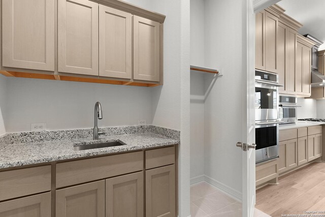 kitchen with baseboards, light stone countertops, stainless steel double oven, gas cooktop, and a sink