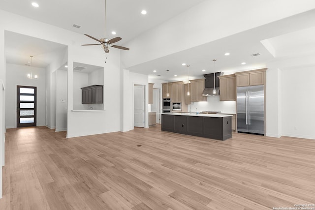 kitchen with open floor plan, light countertops, light wood-style flooring, stainless steel appliances, and wall chimney exhaust hood