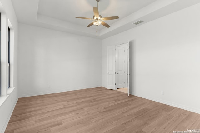 unfurnished room featuring light wood finished floors, visible vents, baseboards, and a tray ceiling