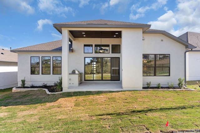 rear view of property featuring a patio area, stucco siding, a shingled roof, and a yard