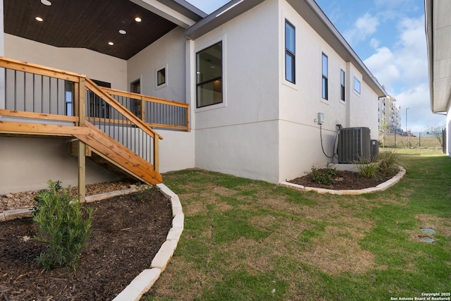 view of property exterior with stucco siding, a lawn, central AC, and stairs