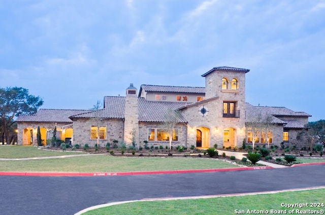 mediterranean / spanish-style house featuring stone siding, a tiled roof, a chimney, and a front yard