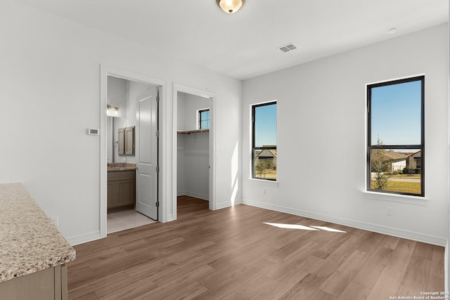 unfurnished bedroom featuring visible vents, baseboards, light wood-style flooring, and a spacious closet