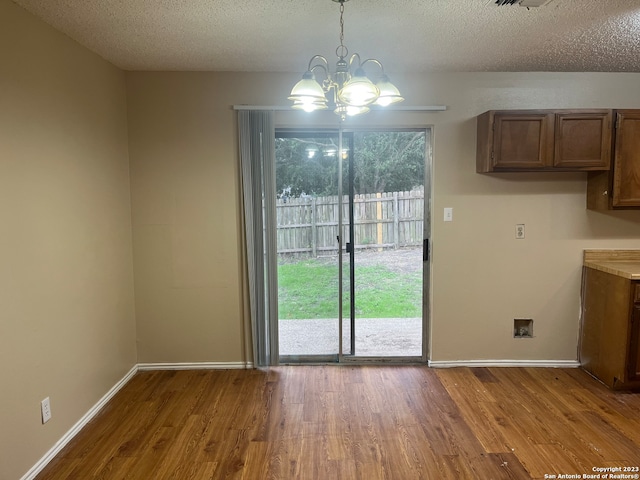 unfurnished dining area featuring a textured ceiling, an inviting chandelier, and wood-type flooring