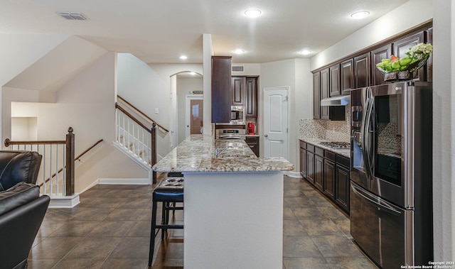 kitchen featuring appliances with stainless steel finishes, decorative backsplash, a breakfast bar, dark brown cabinets, and a center island