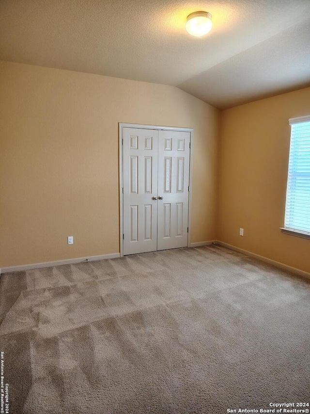 unfurnished bedroom featuring a textured ceiling, a closet, light colored carpet, and vaulted ceiling