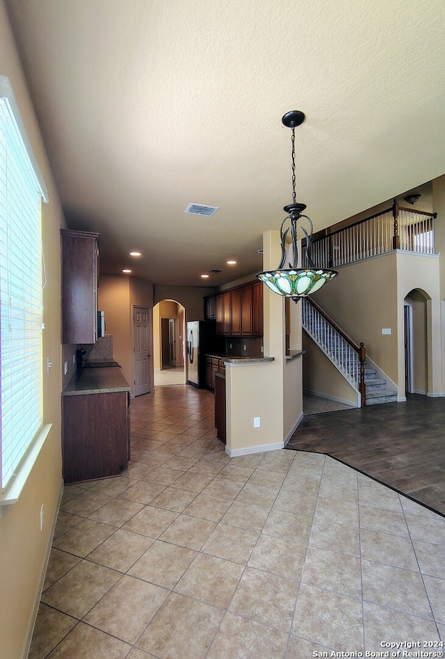 kitchen with stainless steel fridge, light tile patterned floors, dark brown cabinetry, and a wealth of natural light