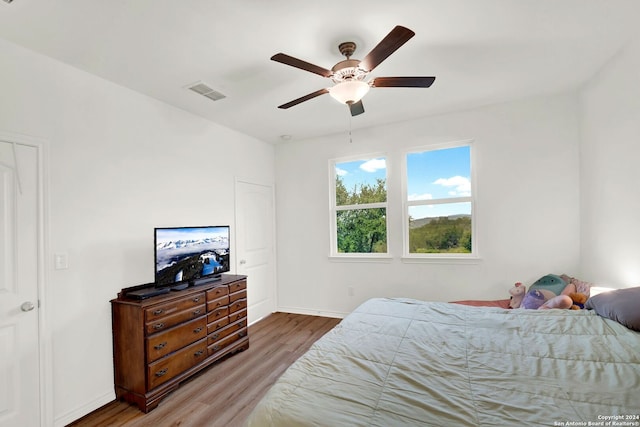 bedroom with a ceiling fan, wood finished floors, visible vents, and baseboards