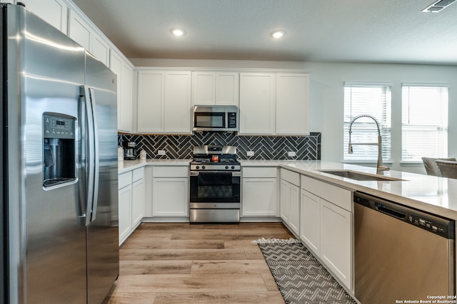 kitchen with appliances with stainless steel finishes, white cabinetry, light hardwood / wood-style flooring, and sink