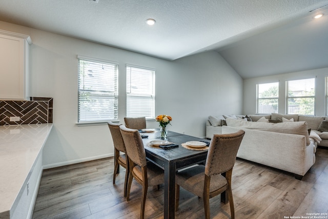 dining area with vaulted ceiling, a textured ceiling, and wood-type flooring