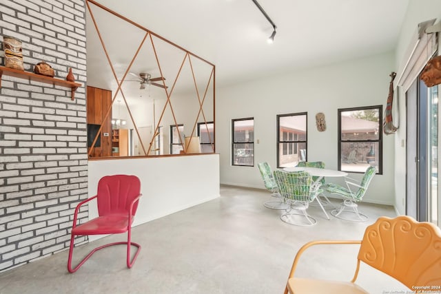 sitting room with track lighting, concrete floors, ceiling fan, and brick wall