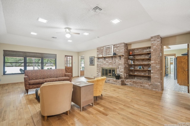 living room with light hardwood / wood-style flooring, ceiling fan, a fireplace, and a textured ceiling