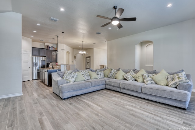 living room featuring light wood-type flooring, ceiling fan with notable chandelier, and sink