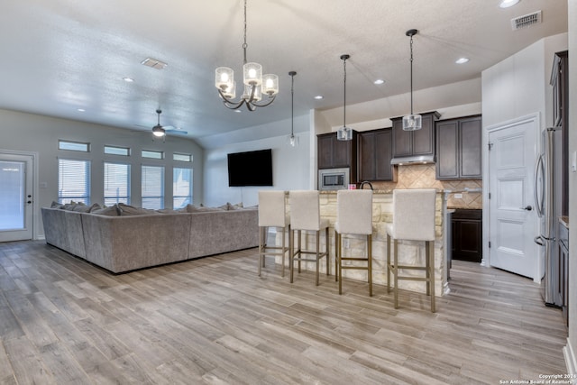 kitchen with a breakfast bar area, ceiling fan with notable chandelier, a center island with sink, light hardwood / wood-style floors, and hanging light fixtures