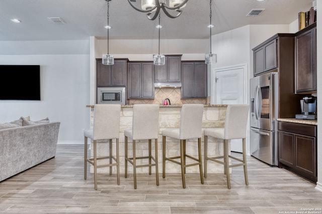 kitchen featuring appliances with stainless steel finishes, a kitchen bar, hanging light fixtures, and light hardwood / wood-style floors