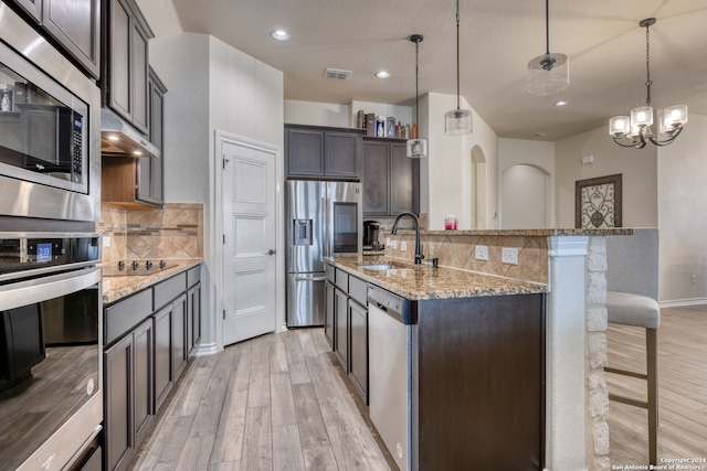 kitchen with decorative light fixtures, stainless steel appliances, sink, and light hardwood / wood-style floors