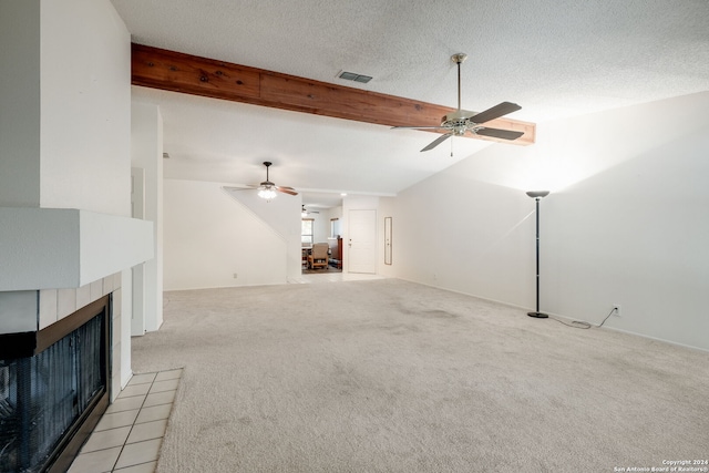 unfurnished living room featuring a textured ceiling, ceiling fan, a tiled fireplace, and vaulted ceiling with beams