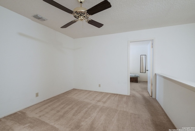 spare room with a textured ceiling, light colored carpet, and ceiling fan