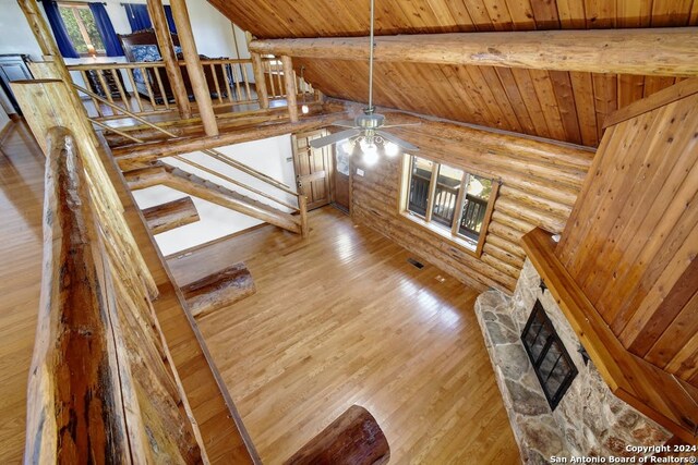 stairs with wood finished floors, lofted ceiling with beams, ceiling fan, a stone fireplace, and wood ceiling