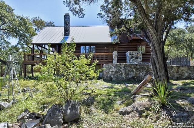 back of house with a wooden deck, log exterior, metal roof, and a chimney