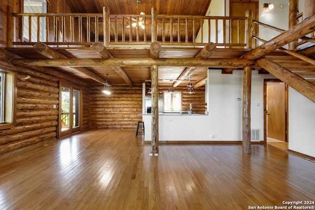 unfurnished living room featuring wood-type flooring, beam ceiling, log walls, and wooden ceiling