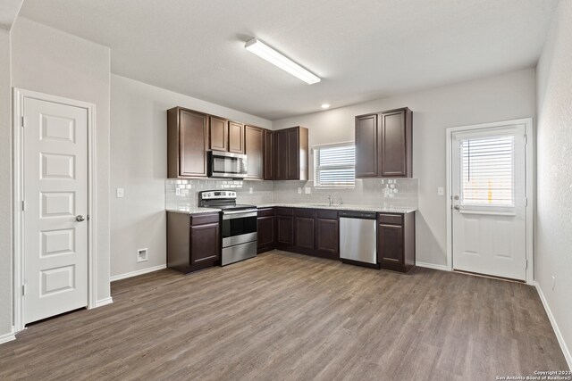 kitchen with dark brown cabinetry, stainless steel appliances, a wealth of natural light, and light hardwood / wood-style flooring