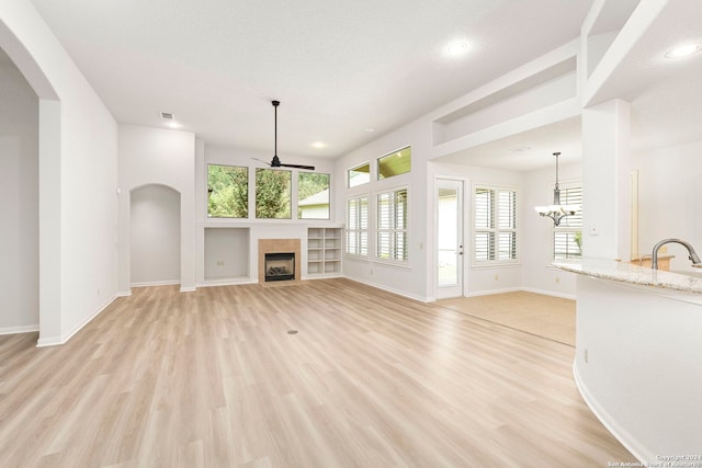 unfurnished living room with arched walkways, a tile fireplace, light wood-type flooring, and ceiling fan