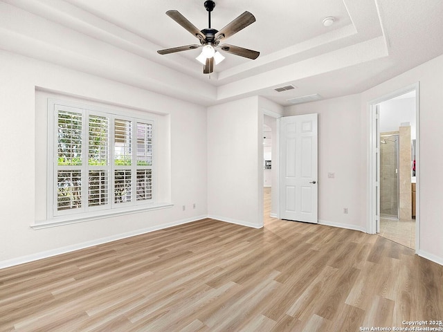 unfurnished bedroom with light wood-type flooring, a tray ceiling, baseboards, and visible vents
