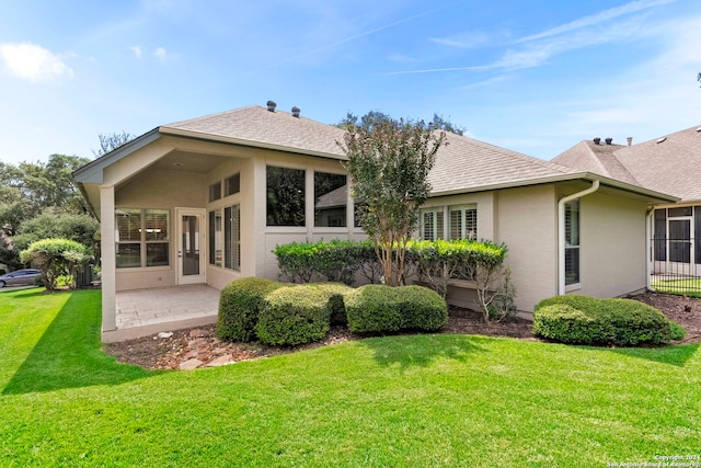 back of house with a yard, roof with shingles, stucco siding, and a patio