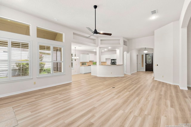 unfurnished living room featuring arched walkways, visible vents, light wood-style flooring, baseboards, and ceiling fan with notable chandelier