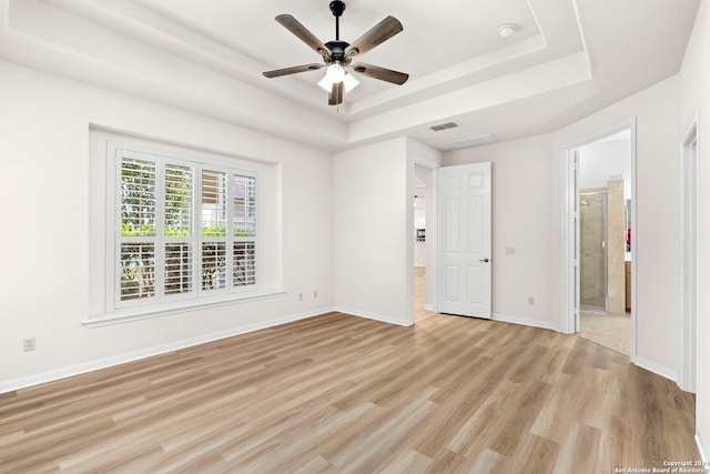 unfurnished bedroom featuring a tray ceiling, baseboards, visible vents, and light wood finished floors