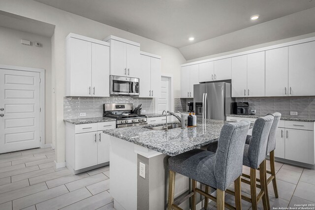 kitchen featuring white cabinets, appliances with stainless steel finishes, light stone countertops, and an island with sink