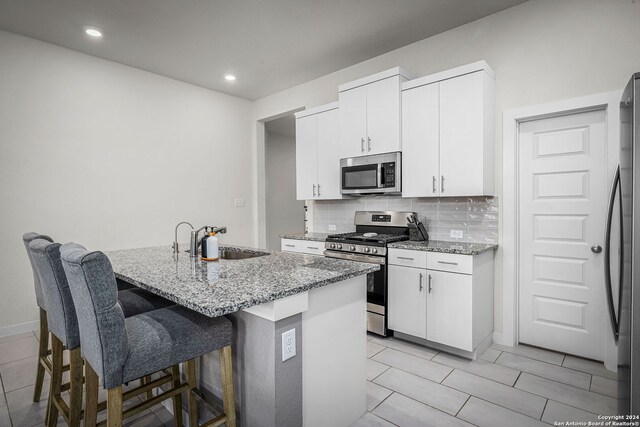 kitchen with appliances with stainless steel finishes, a kitchen island with sink, sink, light stone counters, and white cabinets